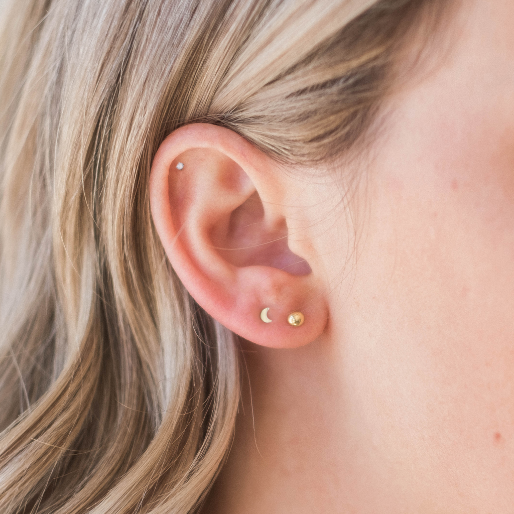 A close-up view of a person's ear with two small earrings, one with a moon symbol and the other with a crescent moon symbol.