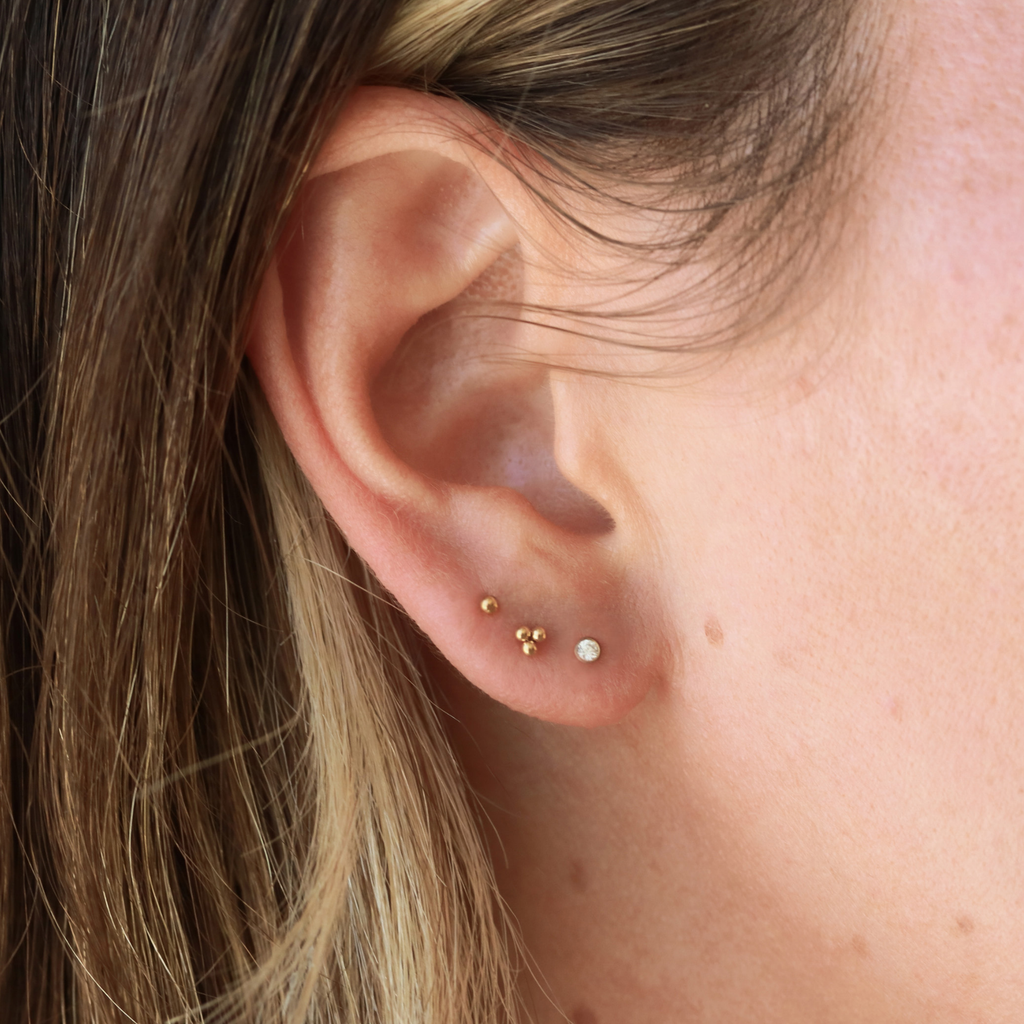A close-up view of a person's ear with three small gold earrings on the earlobe.