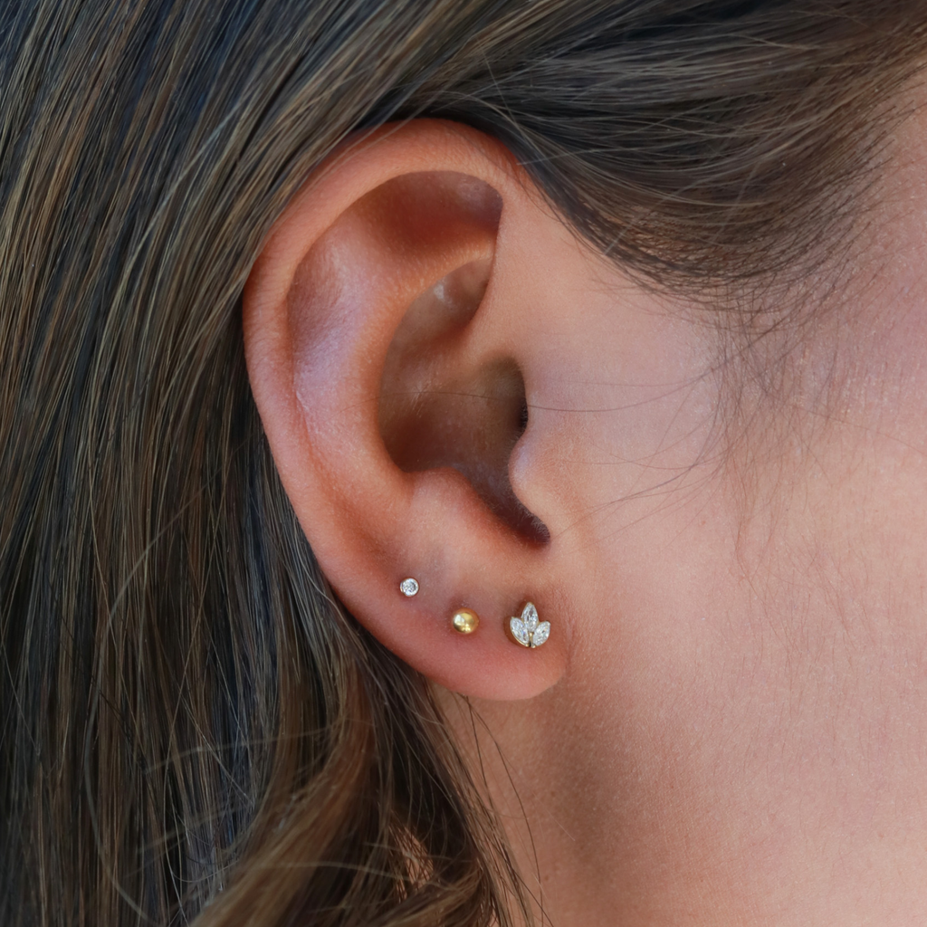 A close-up view of a person's ear adorned with multiple earrings, including three small gold earrings and one larger gold earring.