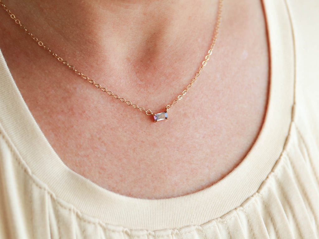 A woman wearing a Baguette Solitaire necklace by Tom Design adorned with a petite birthstone.