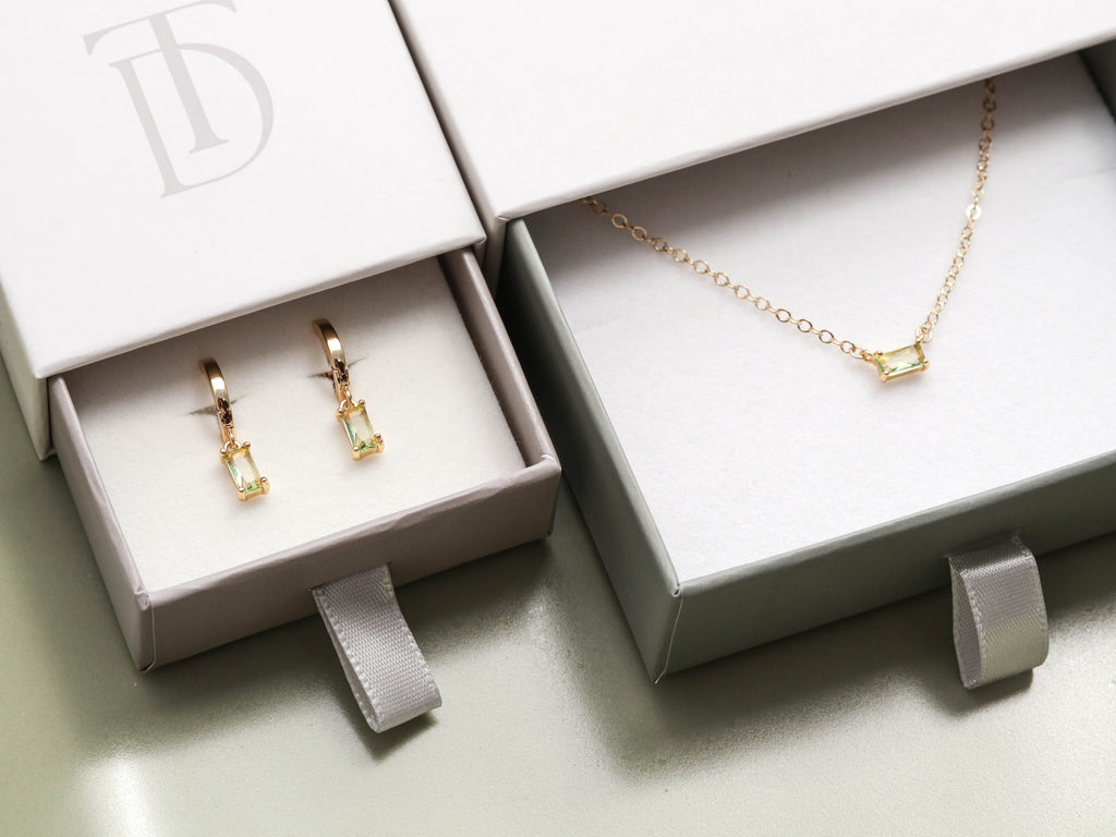 Custom gold birthstone baguette necklace and solitaire earrings in a box.