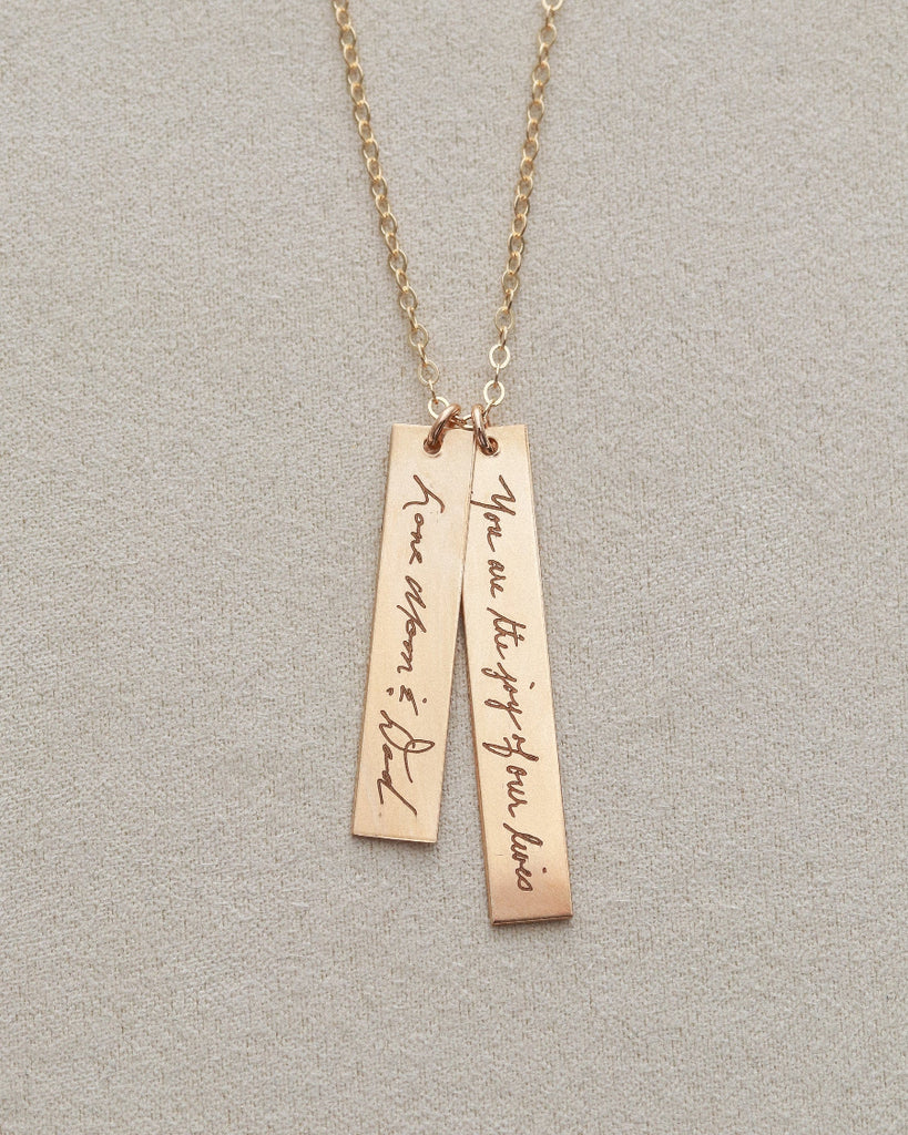 Gold necklace with two vertical pendants on a light gray background